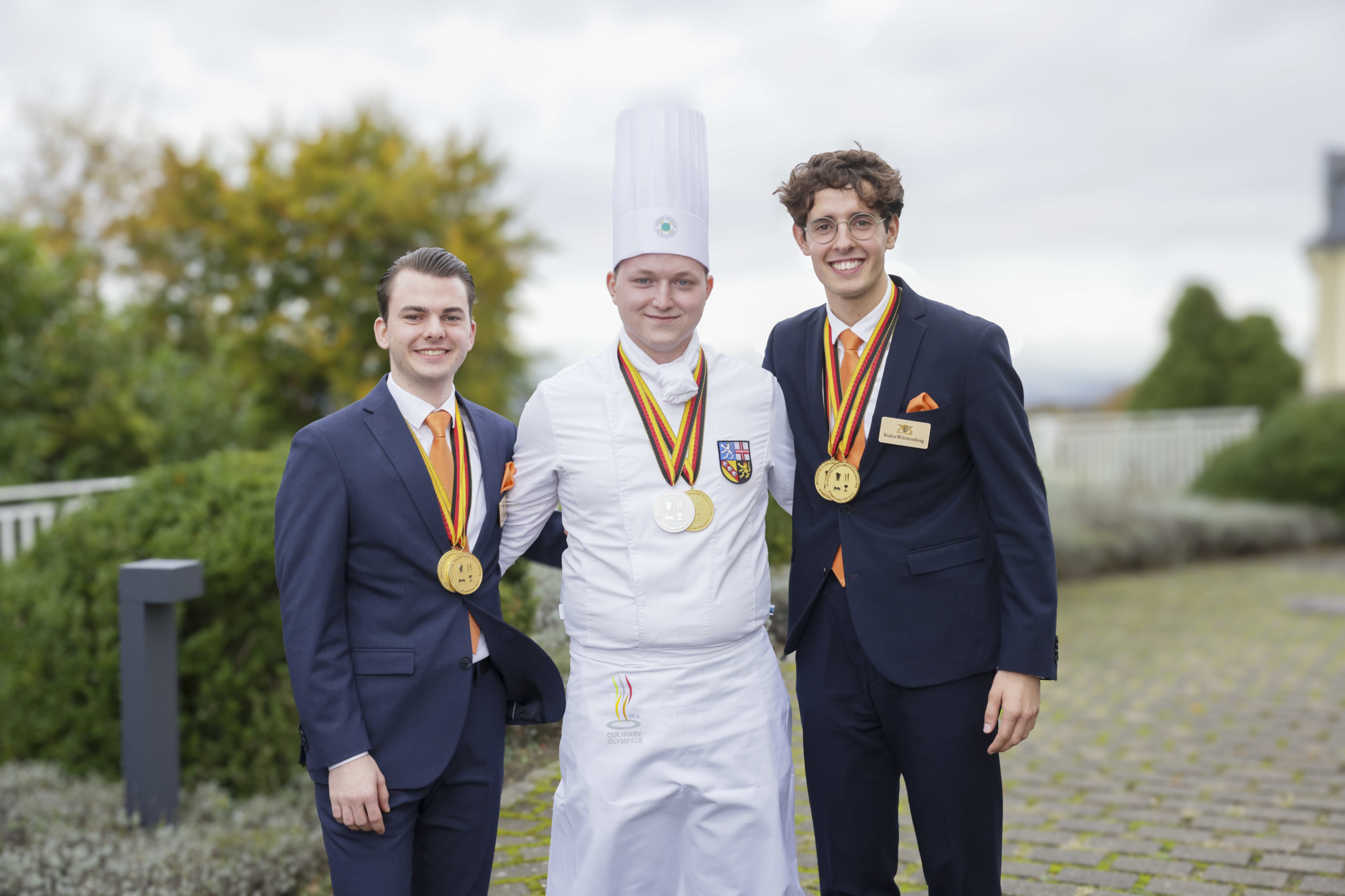 So sehen strahlende Gewinner aus: Hotelfachmann Linus Doufrain (r.) und Restaurantfachmann Johannes Lauth (l.), beide aus Baden-Württemberg, umrahmen Goldkoch Dennis Schneider aus dem Saarland. Foto: Dehoga/Thomas Fedra